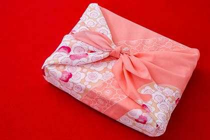 赤い背景にピンクの風呂敷包み。風呂敷には梅の模様が描かれている