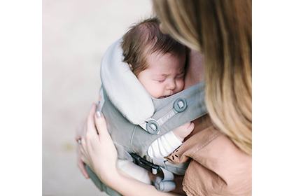 エルゴベビーの抱っこひもをつけた母親に抱っこされて眠る新生児の画像