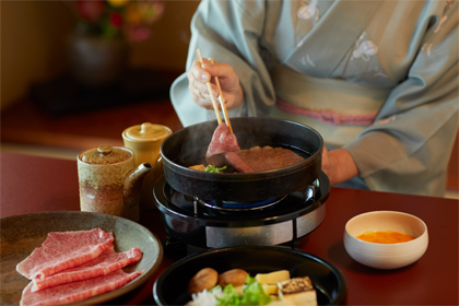 日山 座敷で水色の着物を着た女性がすき焼を作っている