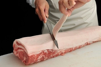 豚の塊肉から余分な脂身を包丁で削いでいる