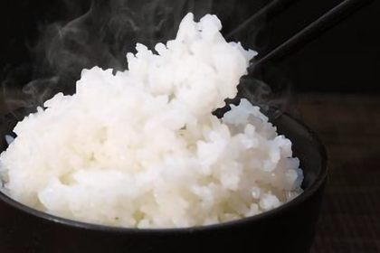 黒い茶碗に炊きたての白米が盛られていて箸で米を掬い上げている画像